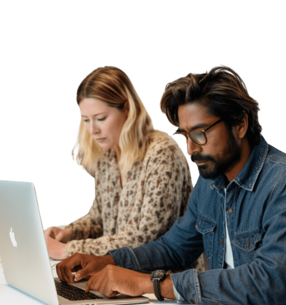 Two people, a woman and a man, are focused on their laptops at a work desk. the man is wearing glasses and a denim jacket, and the woman has blonde hair and a floral top.